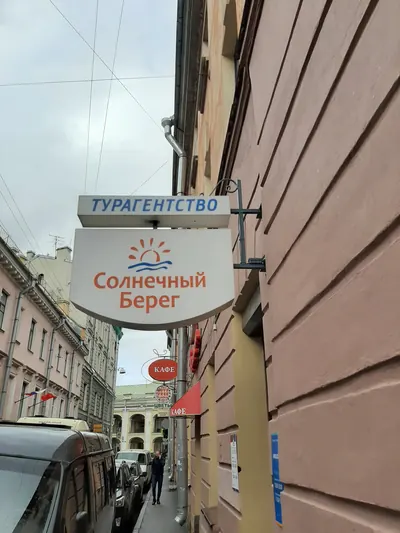 Фигурная консольная вывеска турагентства на кронштейне над тротуаром