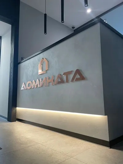 Логотип из объёмных букв под медь на серой стене ресепшена